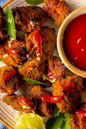Oven Fried Crispy Chicken Popcorn with tomato ketchup and basil leaves served on a white plate