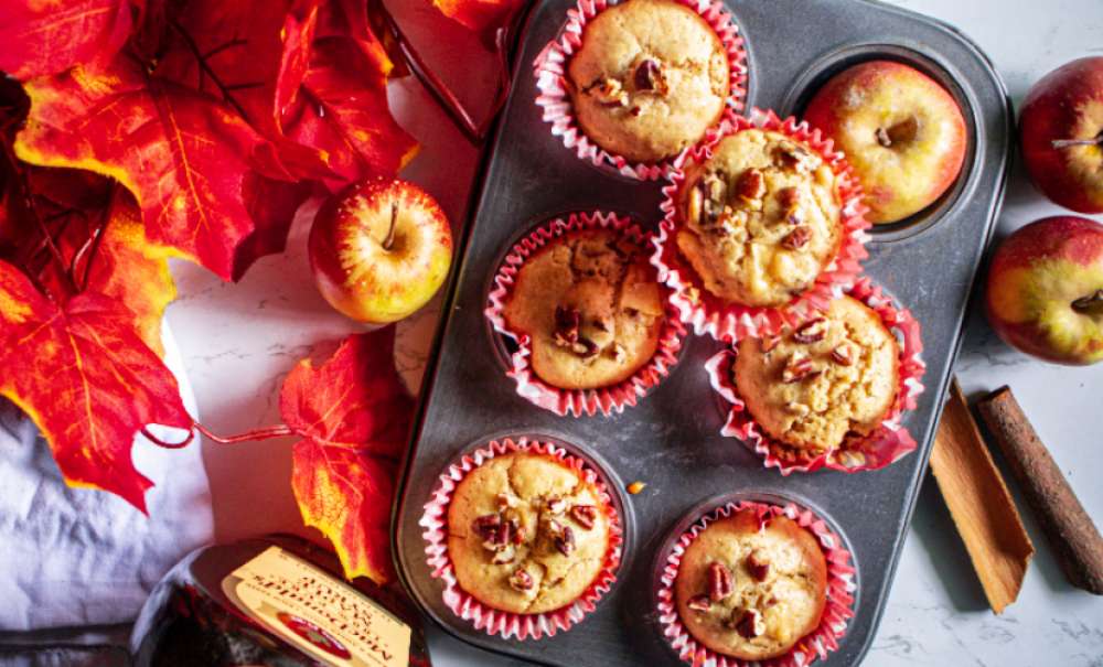 Maple Glazed Apple Cider Pecan Muffins in the muffin tin with fall leaves apples and cinnamon stick beside