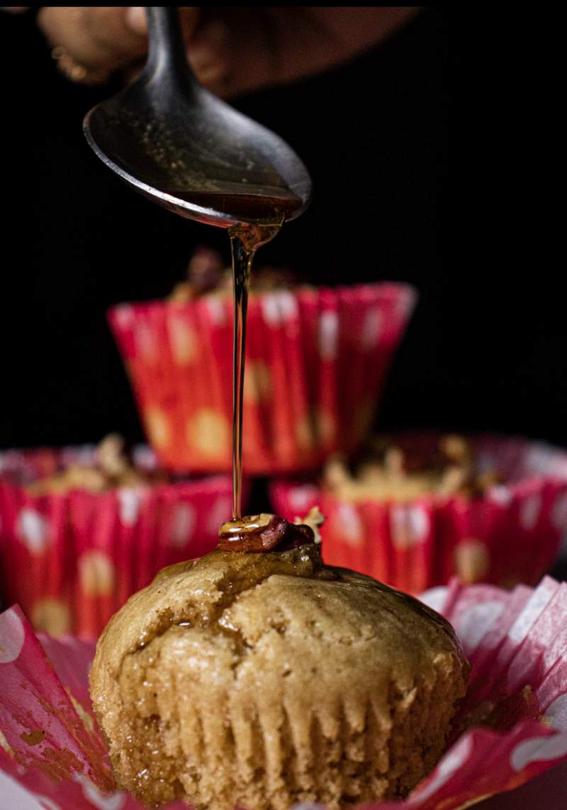 Maple Glazed Apple Cider Pecan Muffins with a spoon pouring maple syrup on the muffin