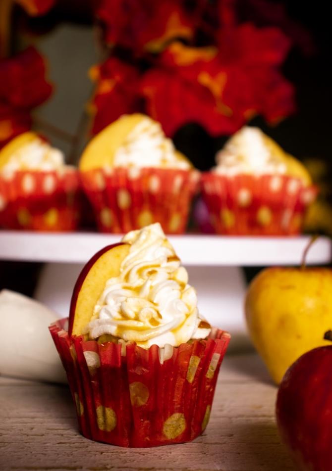 one caramel apple cupcake with an apple slice placed on the frosting. Many other Apple cupcakes placed in the background which are blurred. 