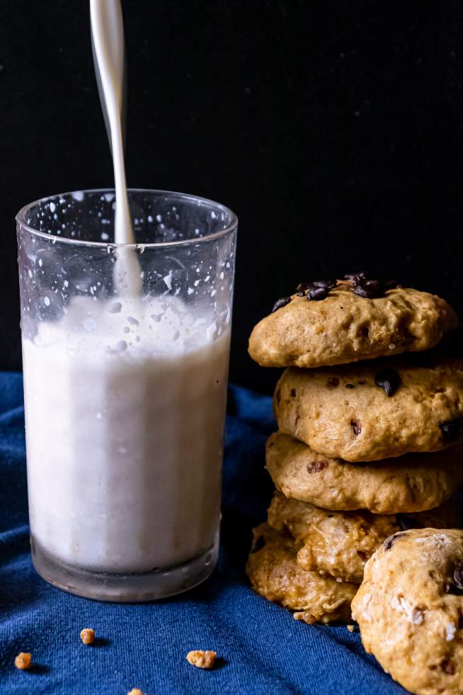 Pouring milk in a glass beside a batch of Soft Pumpkin Chocolate Chip Cookies