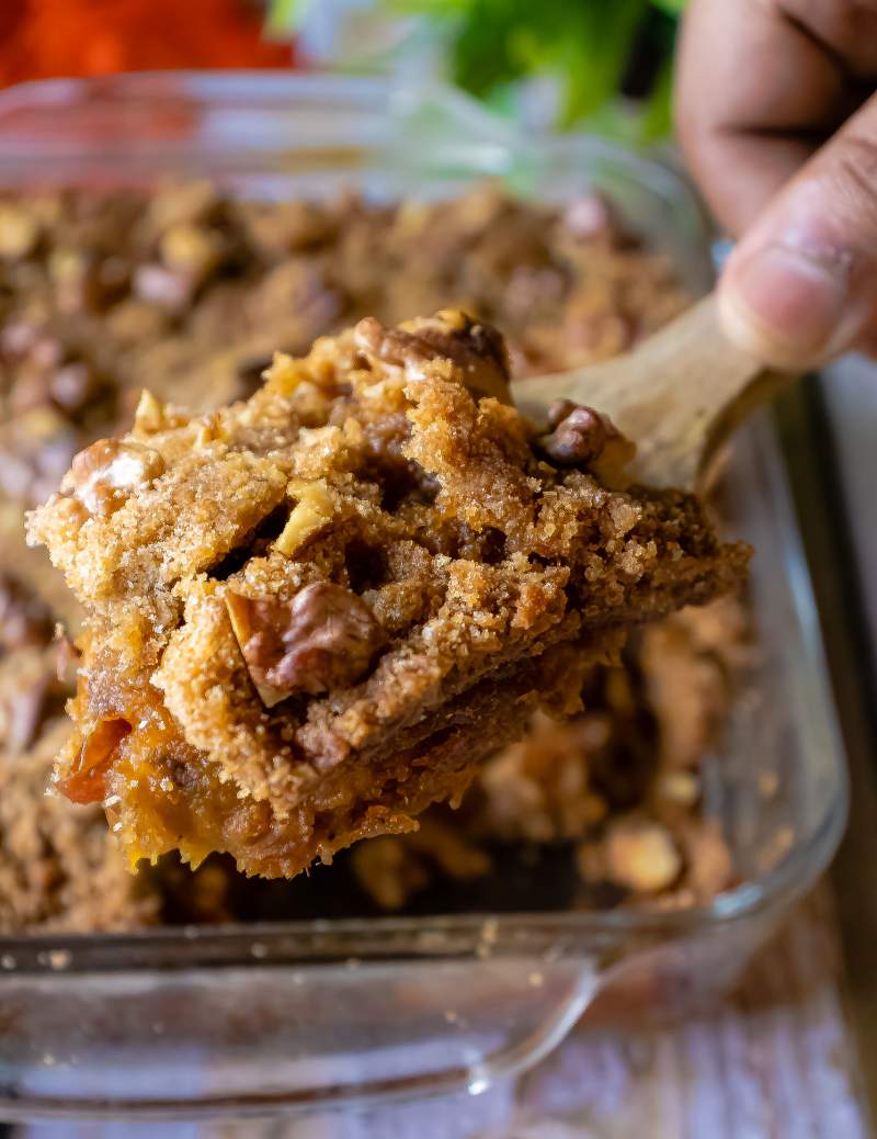 holding a spatula full of sweet potato casserole with casserole dish in the background