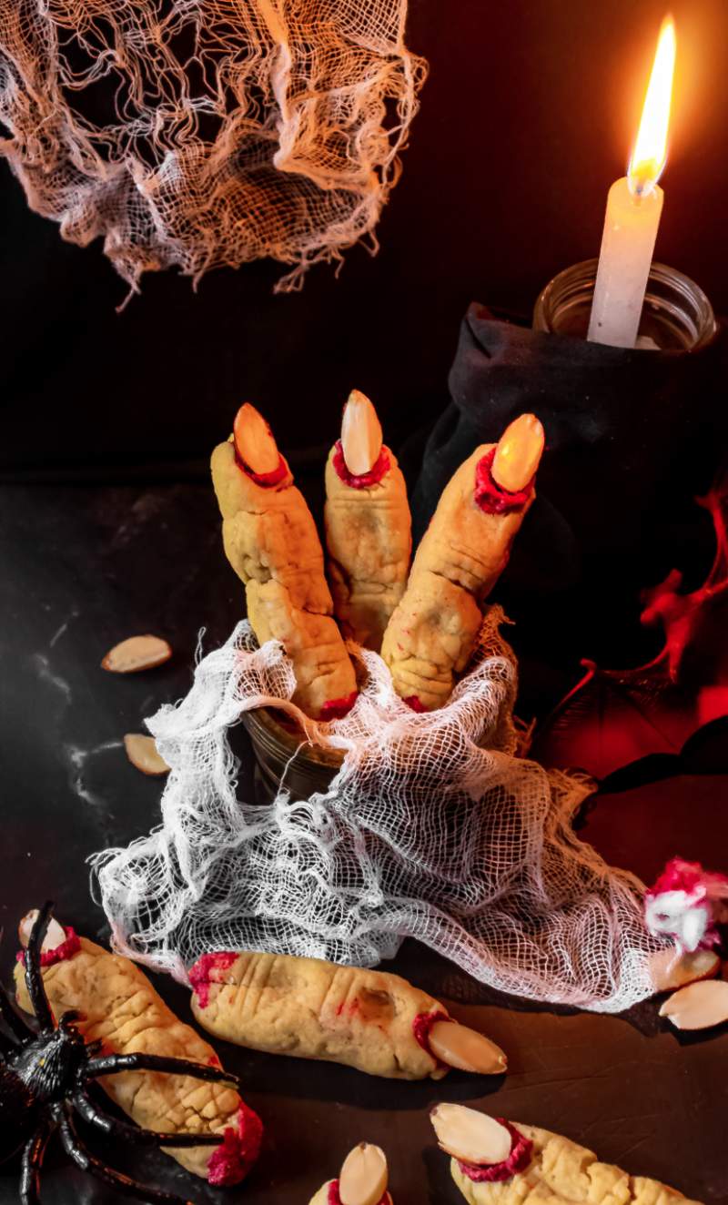 Witchs Finger Sugar Cookies wrapped in bandages and some strewn in front with a spider and bat kept beside it and a candle in the background