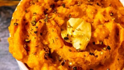 Close up of mashed sweet potato with butter and pepper on top and fall leaves in the background