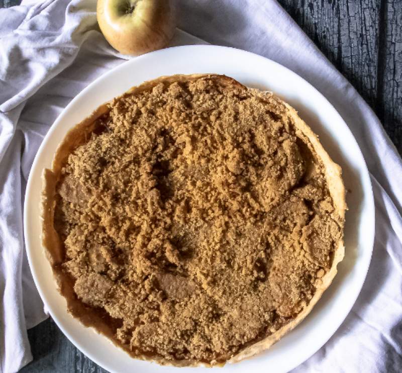 Apple Crumble Pie kept on a white plate with white cloth and an apple in the background