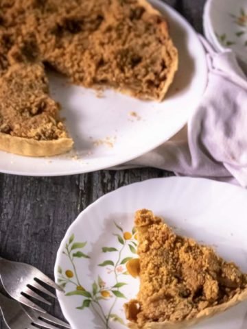 Apple Crumble Pie kept on a white plae with one slice of pie cut and kept in front with fork and a white cloth by its side