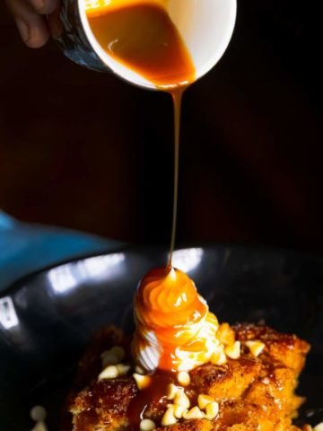 Pouring caramel sauce with a cup on a pumpkin bread pudding kept on a black plate