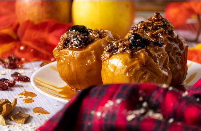 Baked apples on a white plate with fall leaves and cranberries in the back