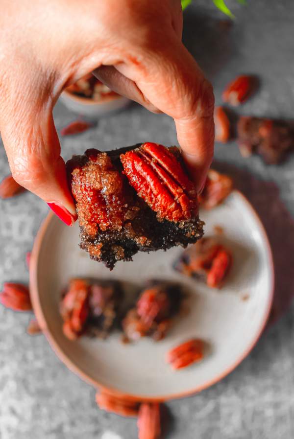 Hands holding one pecan pie brownie in focus while others on the background blurred