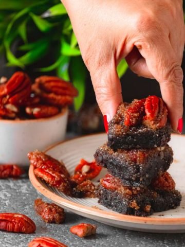 Hands keeping the last brownie on a stack with pecan strewn on the sides