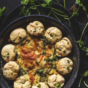 Baked Buttermilk Biscuit Wreath Dip kept in a black plate with cilantro beside it