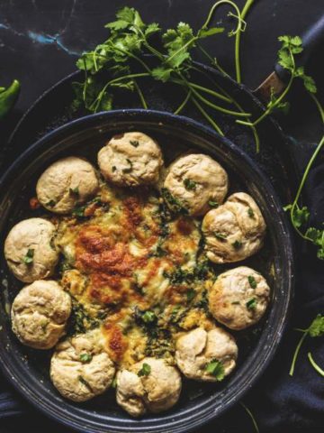 Baked Buttermilk Biscuit Wreath Dip kept in a black plate with cilantro beside it