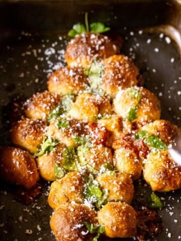 Overhead shot of Christmas tree Pull Apart Appetizer kept on a black baking tray with grated parmesan on its side