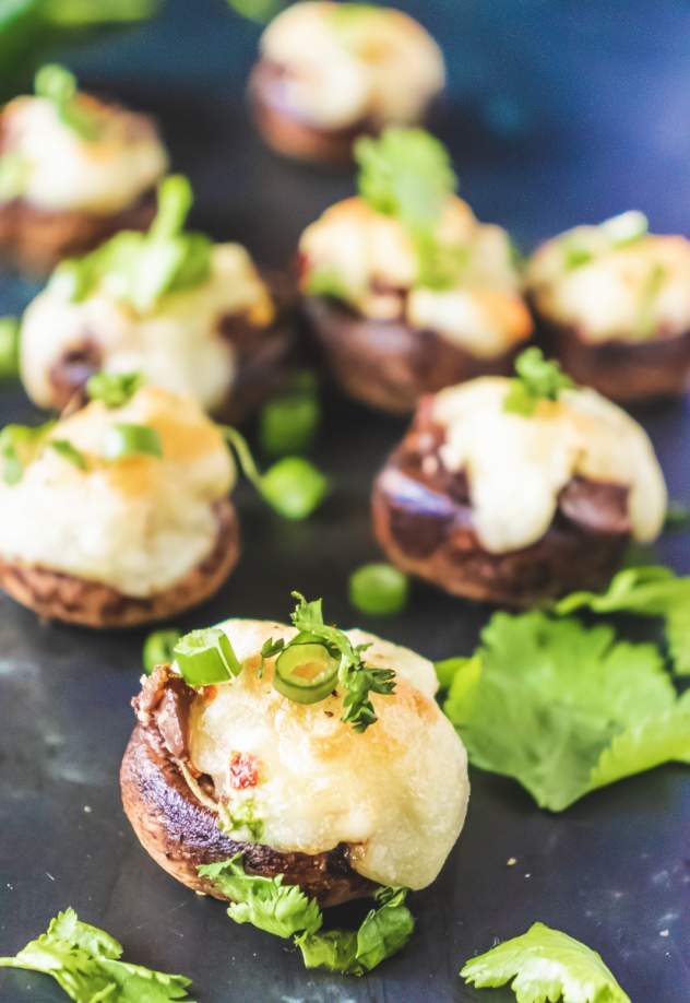 Cream Cheese Stuffed Mushrooms on a black table with few in the background blurred
