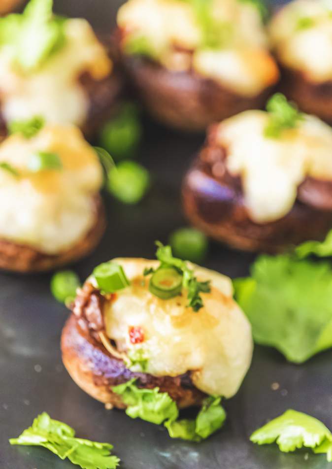 Cream Cheese Stuffed Mushrooms on a black table with cilantro on top and many others in the background 