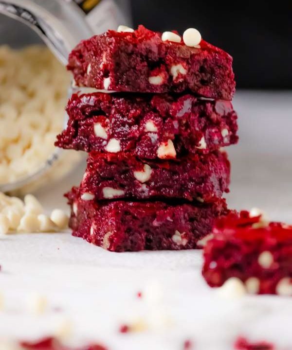 Red Velvet Brownies with White Chocolate Chips arranged in stack with some white chocolate chips on the side