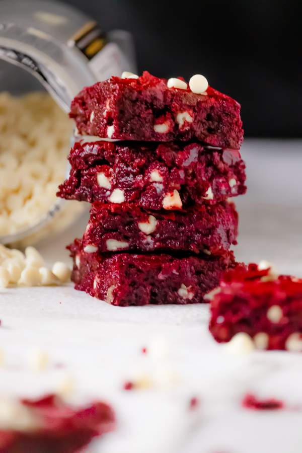 Red Velvet Brownies with White Chocolate Chips arranged in stack with some white chocolate chips on the side