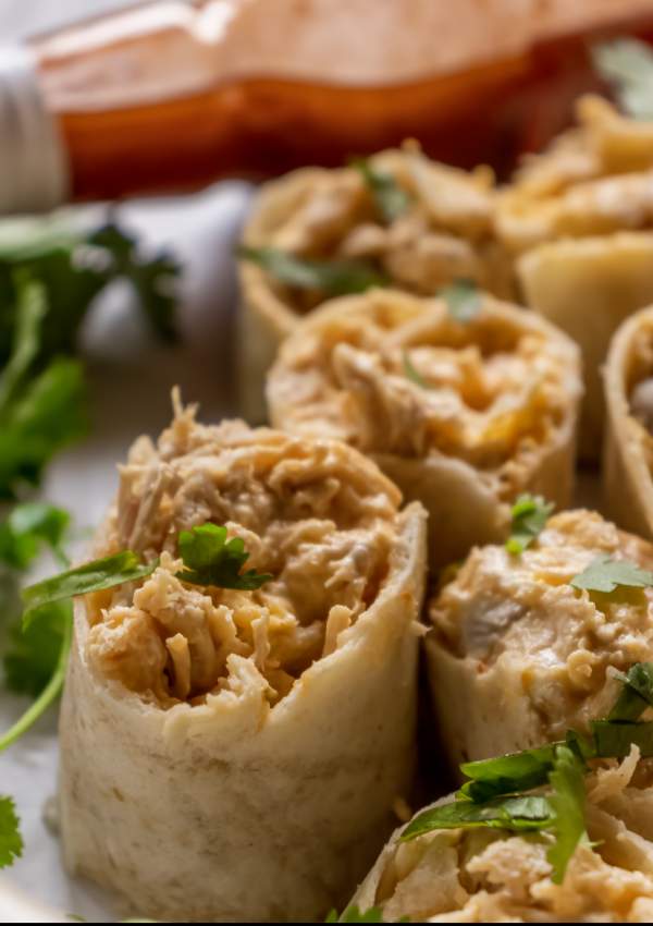ranch cheddar buffalo chicken pinwheels with buffalo sauce in the background