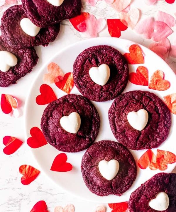 overhead shot of red velvet sugar cookies arranged on a white plate with paper hearts around