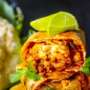 close up of buffalo cauliflower burrito wrap with lime wedges on top