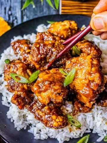 chopsticks picking out one chicken from a plate of orange chicken