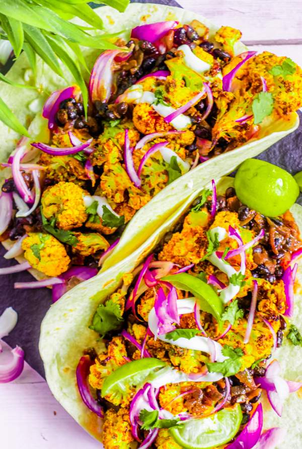ROASTED CAULIFLOWER AND BLACK BEAN TACO WITH LIME WEDGES AND RED ONIONS