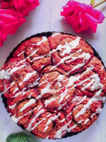 Red Velvet Cinnamon Rolls Recipe from scratch in a plate with roses beside