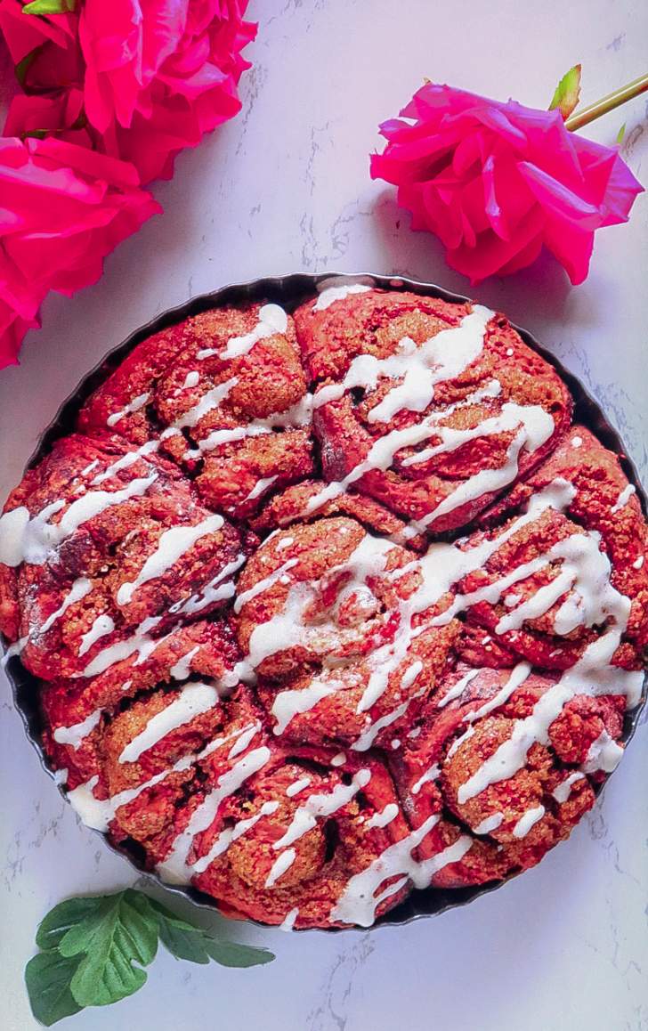Red Velvet Cinnamon Rolls Recipe from scratch in a plate with roses beside 