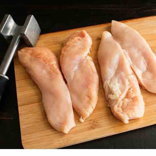 chicken breasts on a wooden table with meat tenderizer