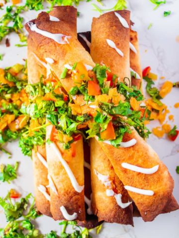 stack of baked cream cheese chicken taquitos with tomatoes, cilantro and cheese on top