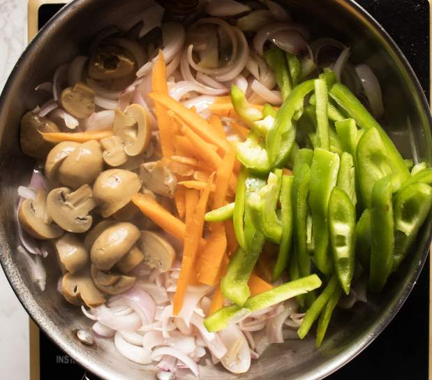 sauteeing mushrooms bell pepper and carrots with onions in a skillet