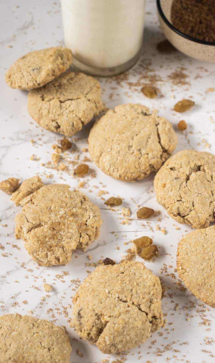 Flourless Oatmeal Raisin Cookies scattered on a white background with raisins and milk