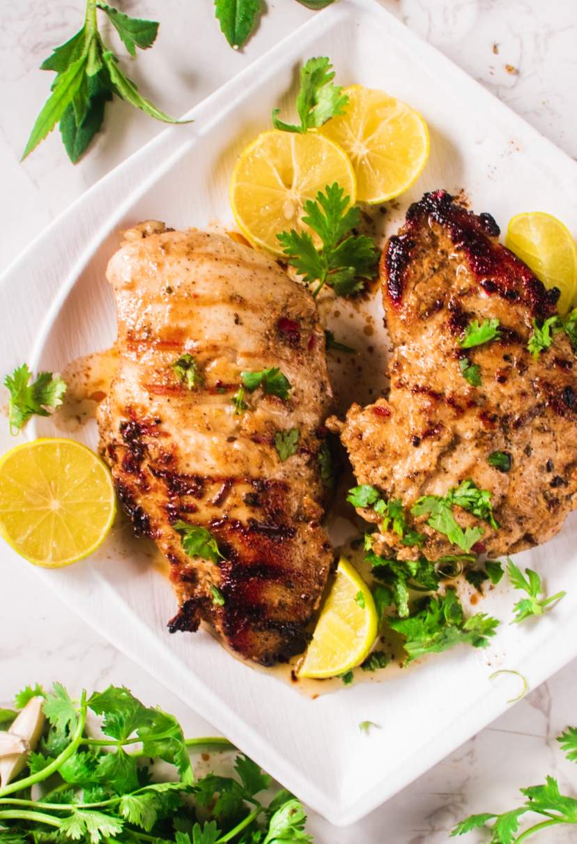 Greek Grilled Chicken kept on a white plate with lemon wedges and cilantro