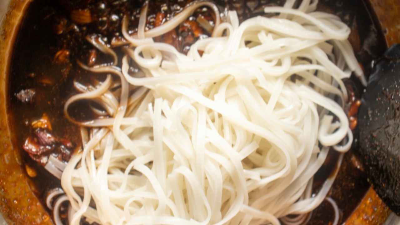 adding cooked rice noodles to sauce in the skillet