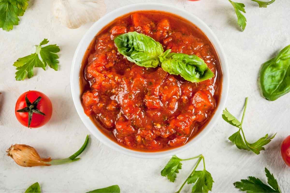 marinara sauce in a white bowl with basil and parsley around it