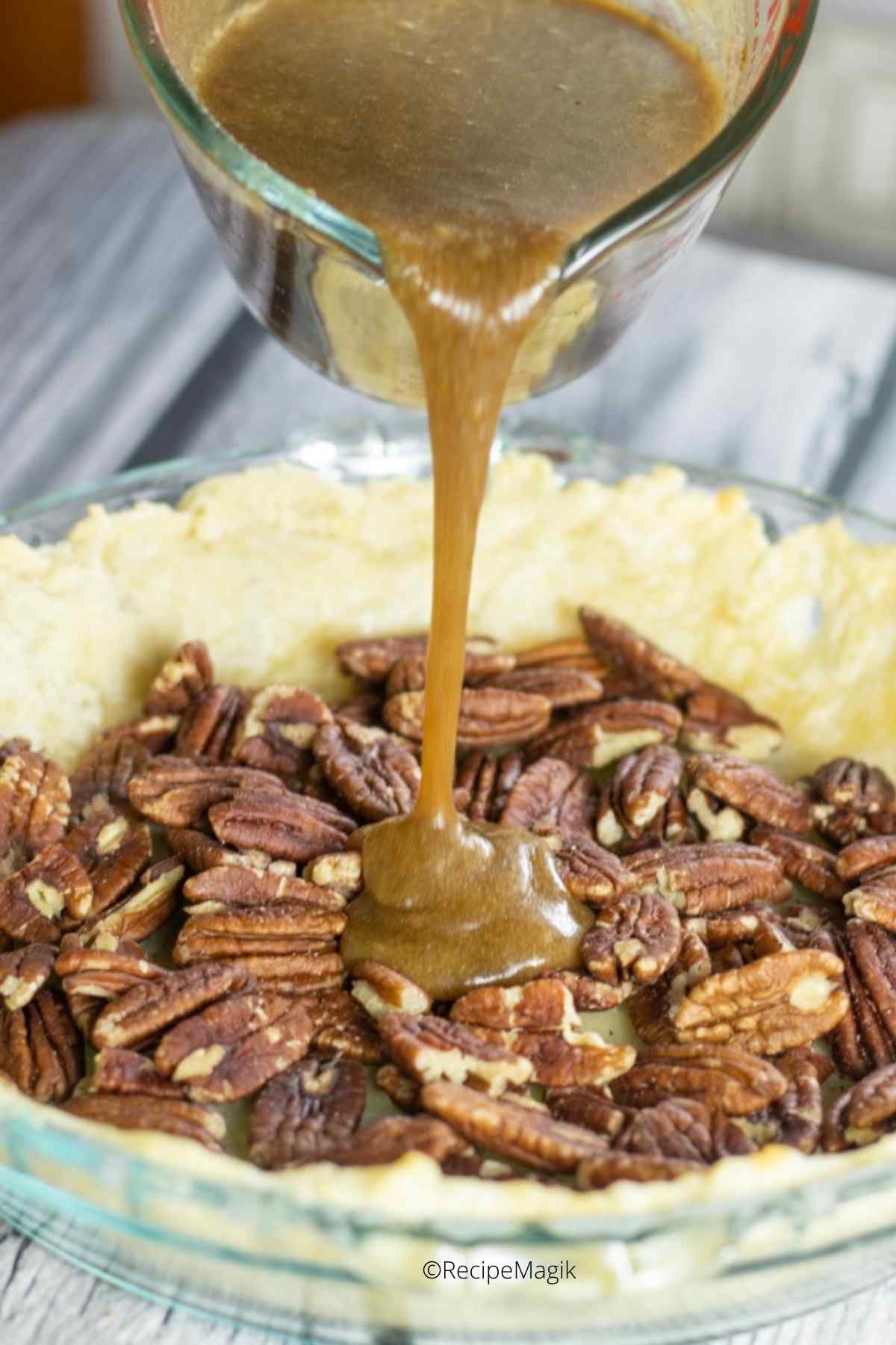 pouring pecan pie filling into the pie crust over pecan nuts