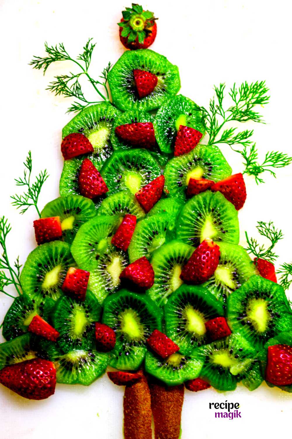 Christmas tree fruit platter with fresh fruits and dill leaves arranged on a white board
